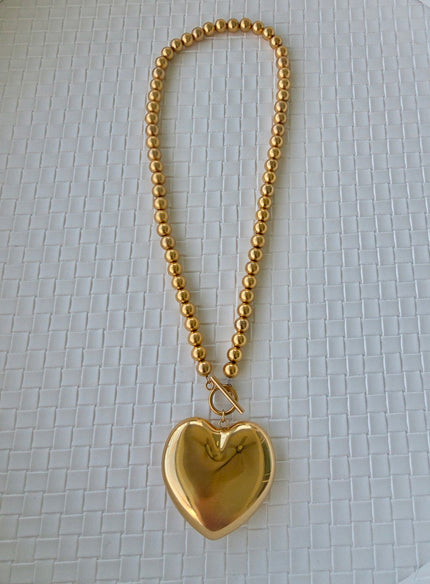 Gold heart-shaped pendant on a chain against a textured white background