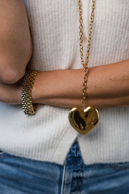 Gold heart-shaped pendant necklace worn by a person with a white sweater and blue jeans.