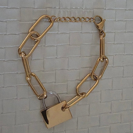 Gold chain bracelet with a gold and silver padlock charm on a textured gray background
