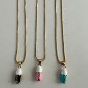 three separate gold chain pendants holding a pink, tiffany blue and black colored pill charm with the word chill written in gold letters on the pill charm