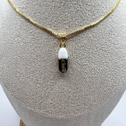 gold chain pendant holding a black colored pill charm with the word chill written in gold letters on the pill charm