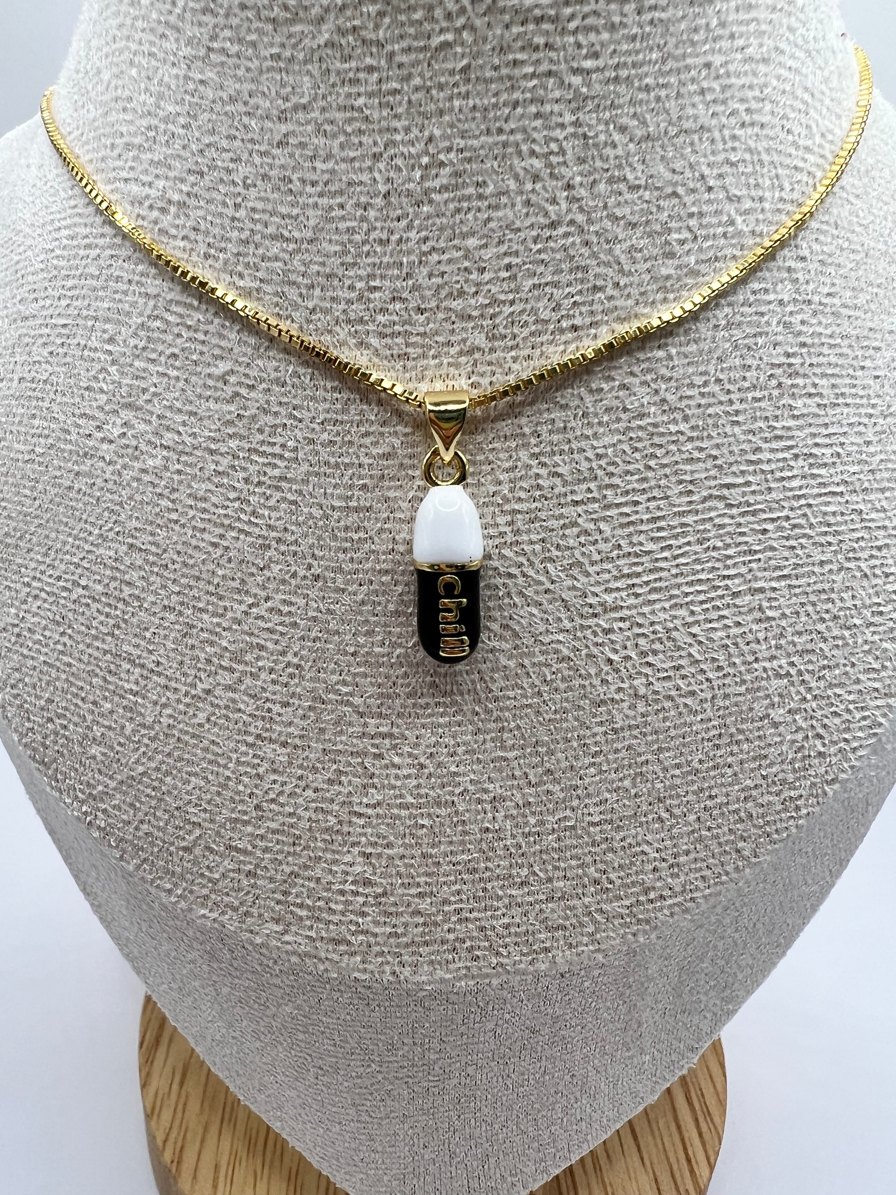 gold chain pendant holding a black colored pill charm with the word chill written in gold letters on the pill charm