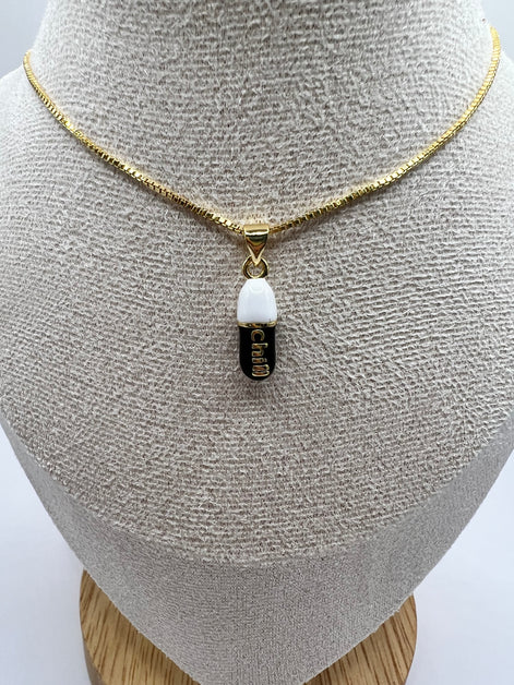 gold chain pendant holding a black colored pill charm with the word chill written in gold letters on the pill charm