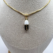 gold chain pendant holding a black colored pill charm with the word chill written in gold letters on the pill charm