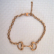 Gold chain snaffle bit necklace on a white background