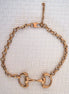Gold chain snaffle bit necklace on a white background
