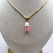 gold chain pendant holding a pink colored pill charm with the word chill written in gold letters on the pill charm