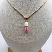 gold chain pendant holding a pink colored pill charm with the word chill written in gold letters on the pill charm