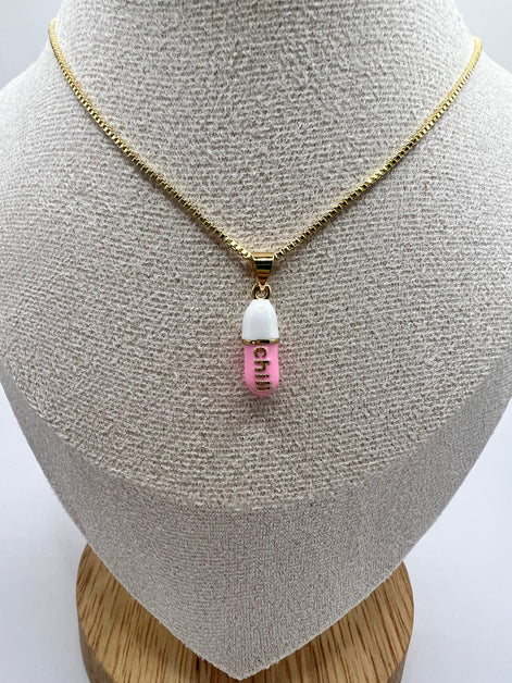 gold chain pendant holding a pink colored pill charm with the word chill written in gold letters on the pill charm