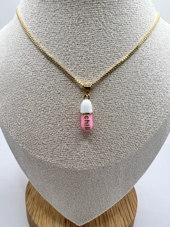 gold chain pendant holding a pink colored pill charm with the word chill written in gold letters on the pill charm