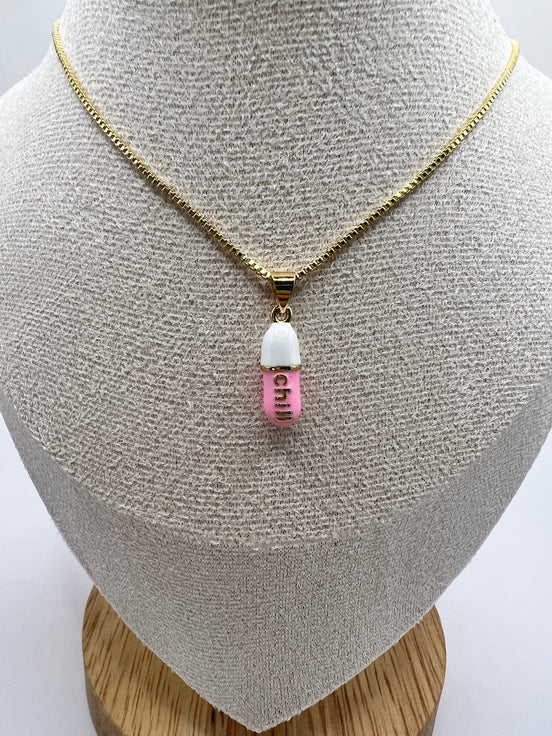 gold chain pendant holding a pink colored pill charm with the word chill written in gold letters on the pill charm