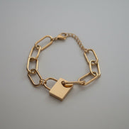 Gold chain bracelet with a padlock charm on a white background