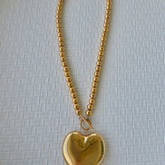 Gold heart-shaped pendant on a chain against a textured white background