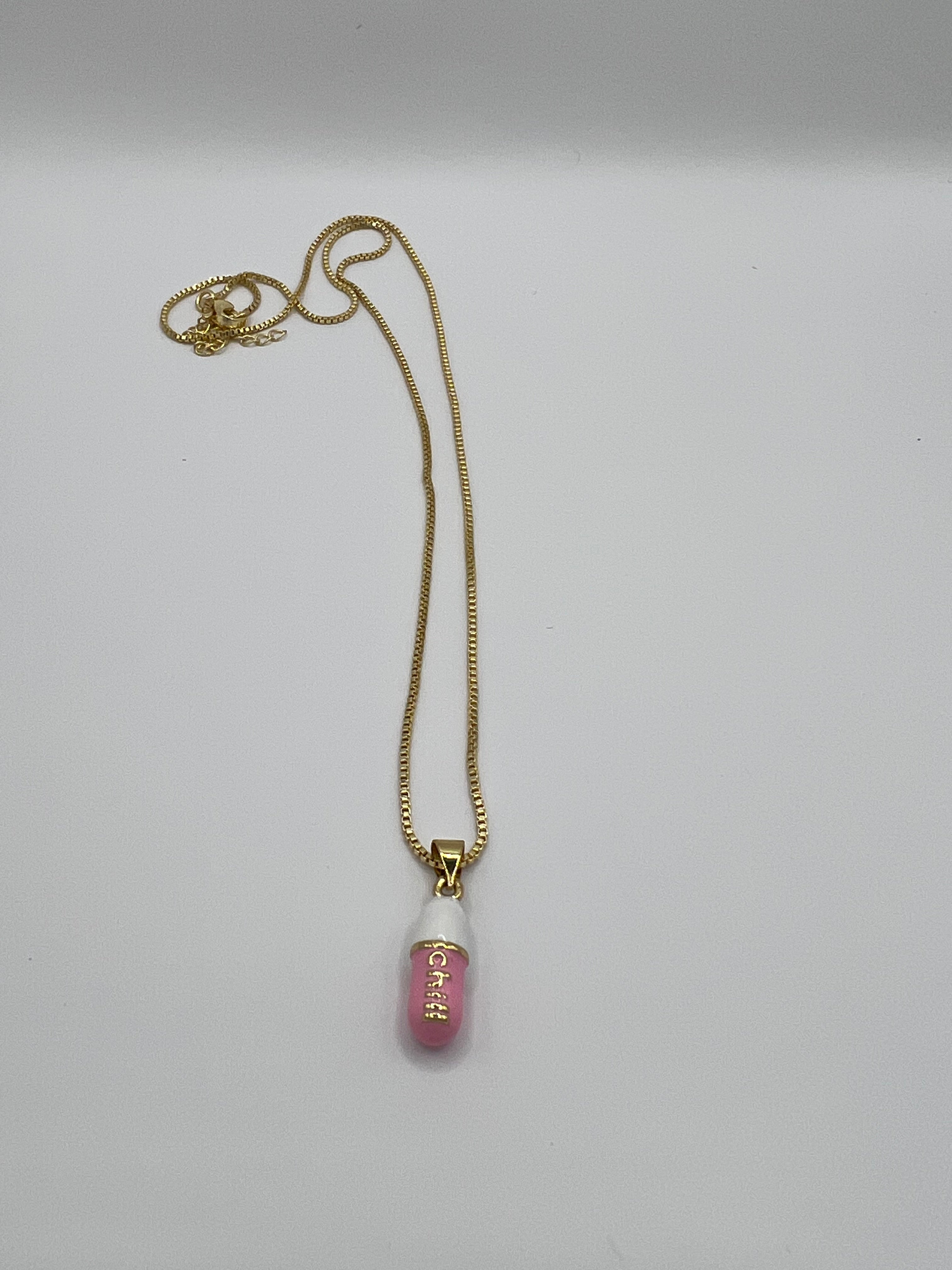 gold chain pendant holding a pink colored pill charm with the word chill written in gold letters on the pill charm