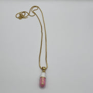 gold chain pendant holding a pink colored pill charm with the word chill written in gold letters on the pill charm