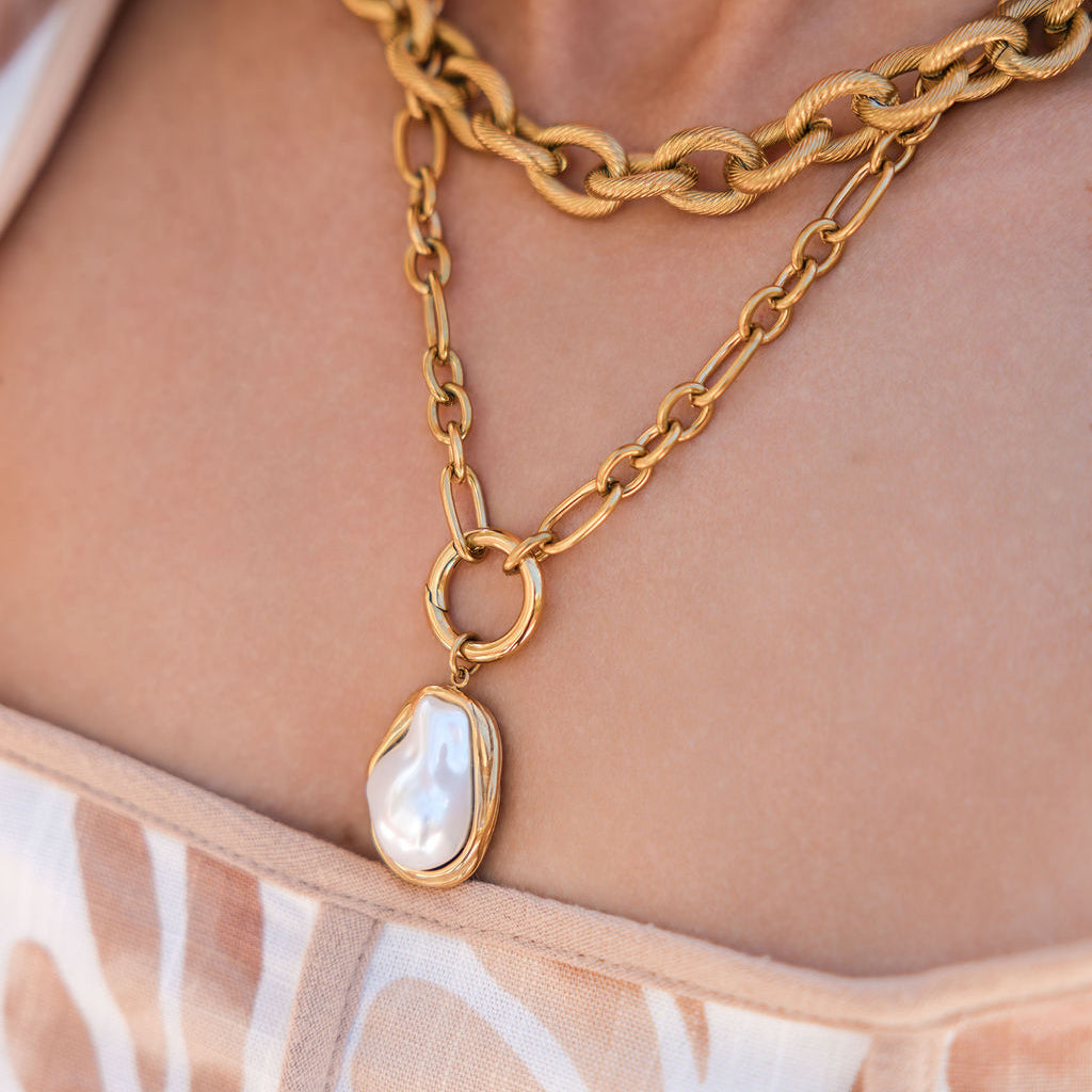 Gold chain necklace with a pendant on a person wearing a floral top.