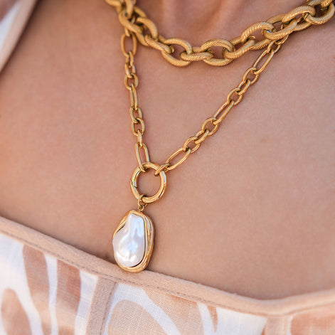 Gold chain necklace with a pendant on a person wearing a floral top.