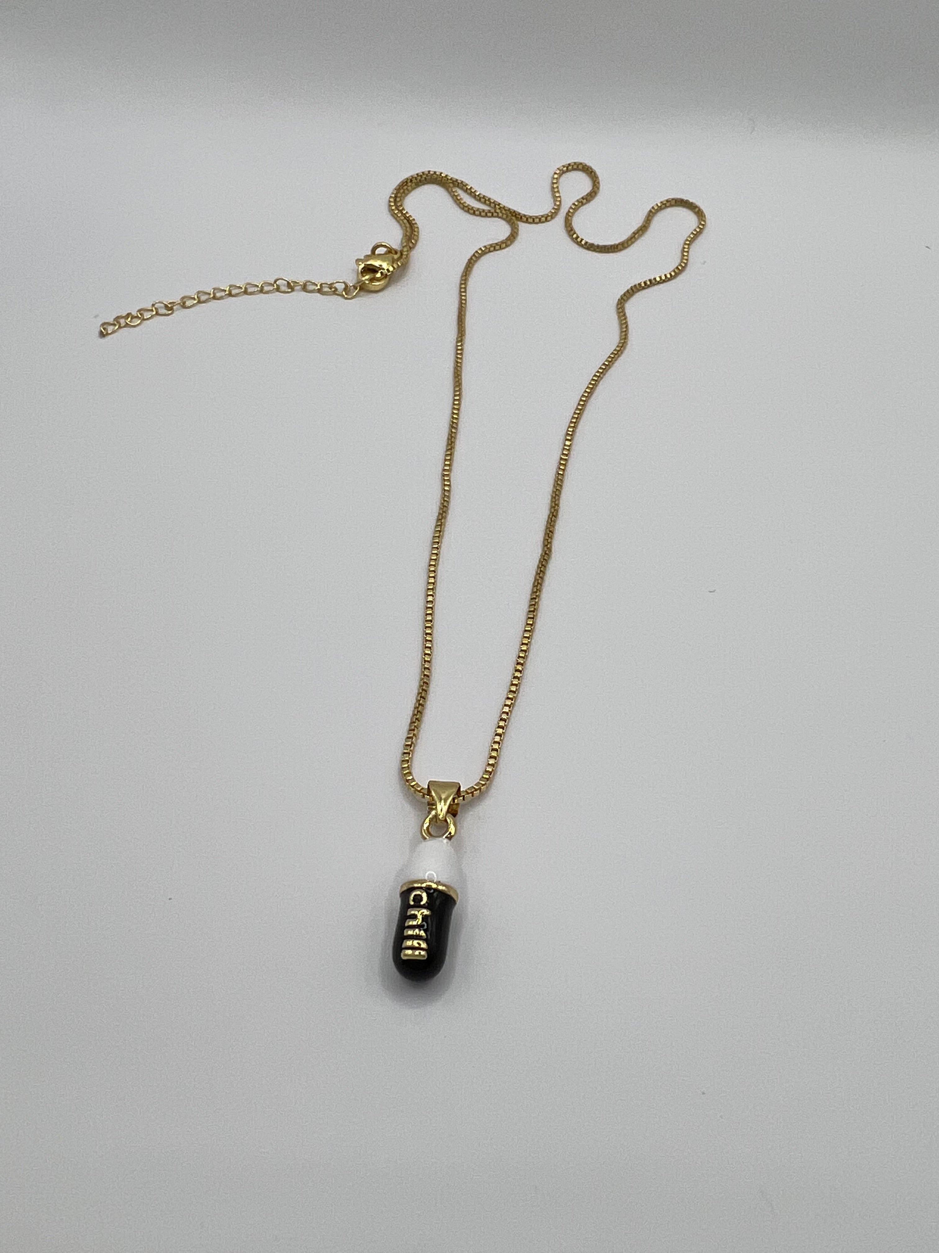 gold chain pendant holding a black colored pill charm with the word chill written in gold letters on the pill charm