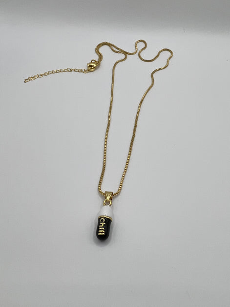 gold chain pendant holding a black colored pill charm with the word chill written in gold letters on the pill charm