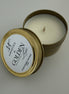 Gold candle tin with a white candle inside on a textured white surface