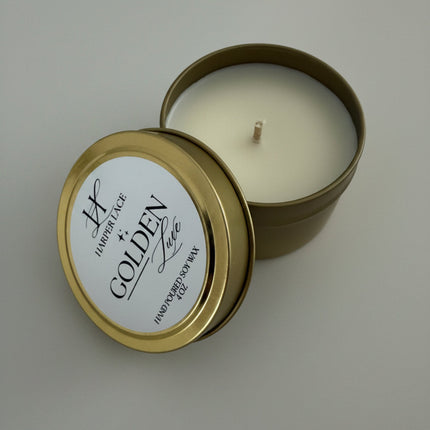 Gold candle tin with a white candle inside on a textured white surface