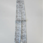 Greige toile floral-patterned silk scarf on a white surface