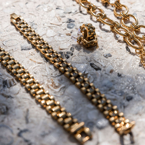 Gold chain bracelet and earrings on a textured surface
