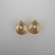 Gold earrings with a central gemstone on a gray woven surface