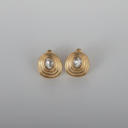 Gold earrings with a central gemstone on a gray woven surface