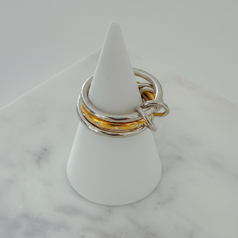 Three rings stacked on top of each other, with the top two rings in gold color and the bottom one in silver, displayed on a white stand on a marble surface.