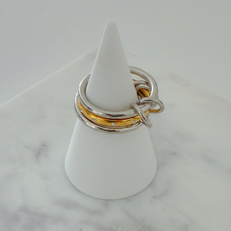 Three rings stacked on top of each other, with the top two rings in gold color and the bottom one in silver, displayed on a white stand on a marble surface.