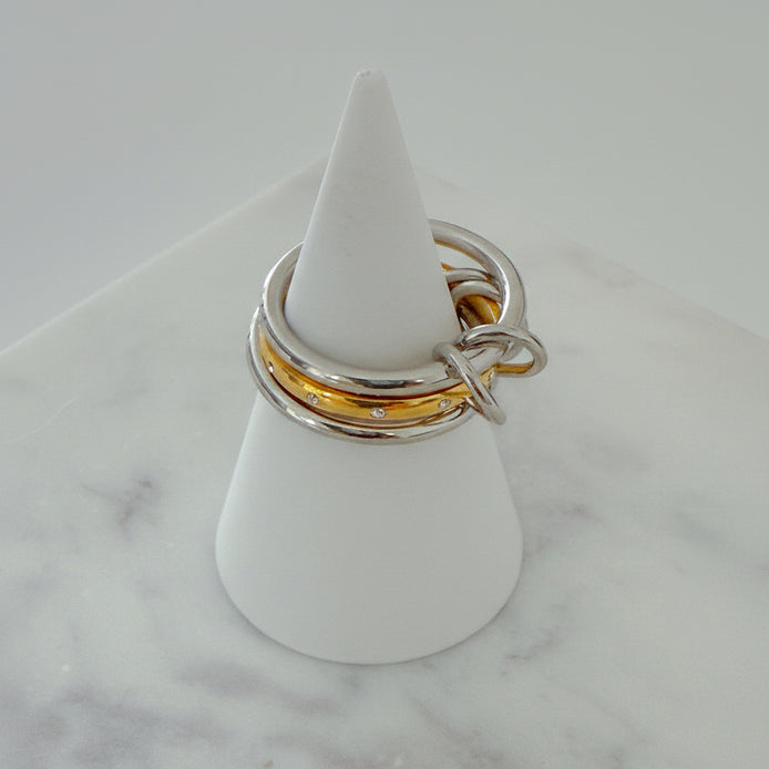 Three rings stacked on top of each other, with the top two rings in gold color and the bottom one in silver, displayed on a white stand on a marble surface.