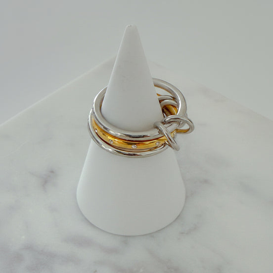 Three rings stacked on top of each other, with the top two rings in gold color and the bottom one in silver, displayed on a white stand on a marble surface.