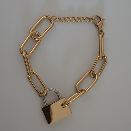Gold chain bracelet with a gold and silver padlock charm on a textured gray background